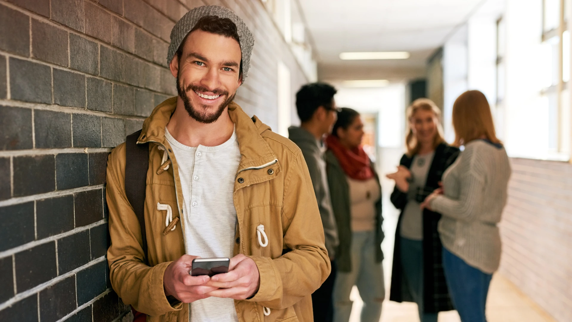Glad kille med mobil i händerna i skolkorridor